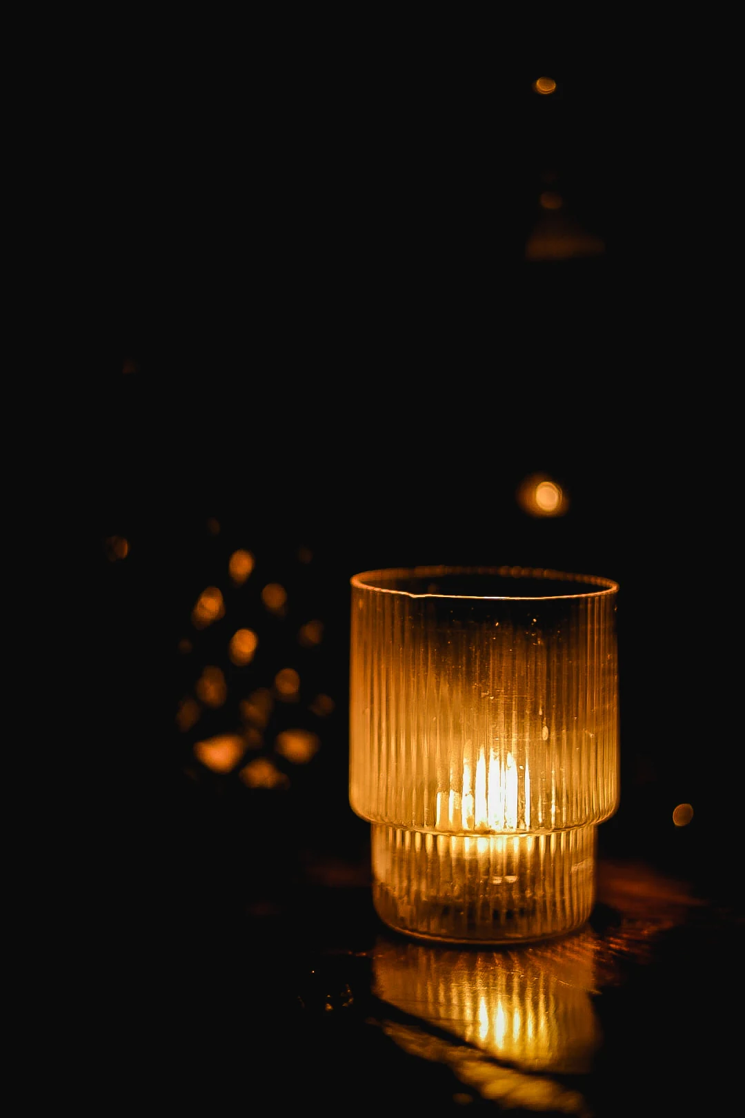 Amber candlelight in a ribbed glass holder reflected on the dark wooden bar.