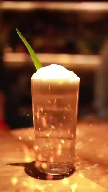 Bartender finishing a tall cocktail with foam and a green garnish.