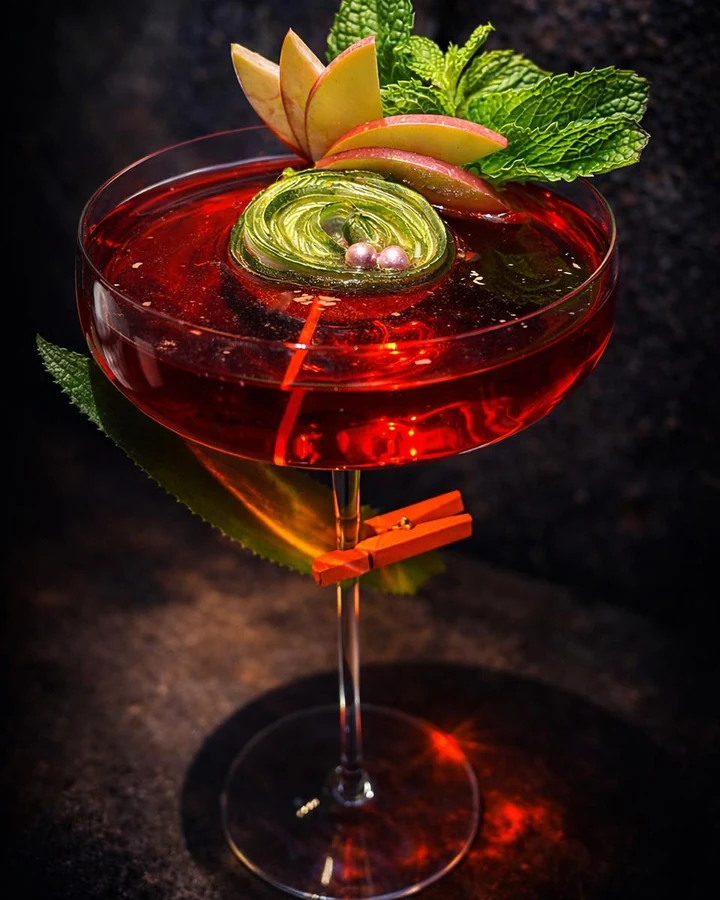 Red cocktail garnished with apple slices and fresh mint.