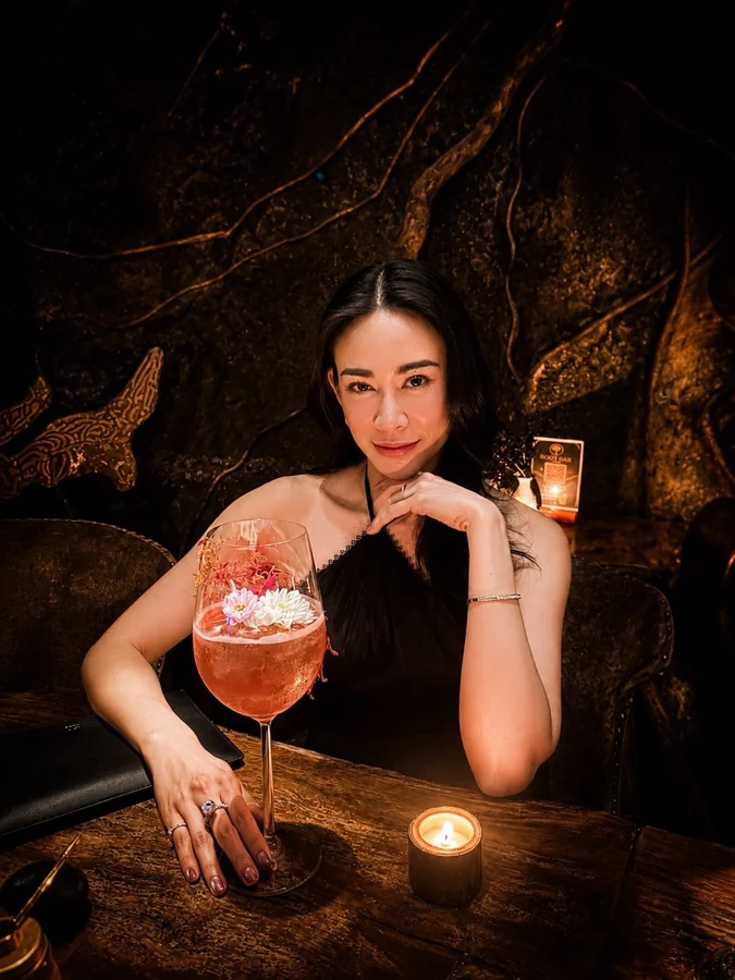 Guest beside a floral cocktail at a candlelit Root Bar table.