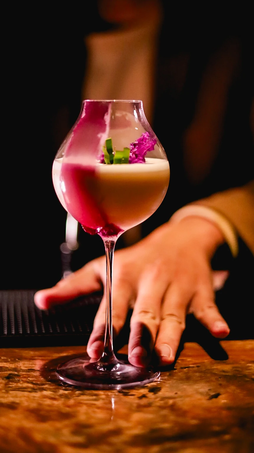 A Root Bar bartender presenting a pink cocktail