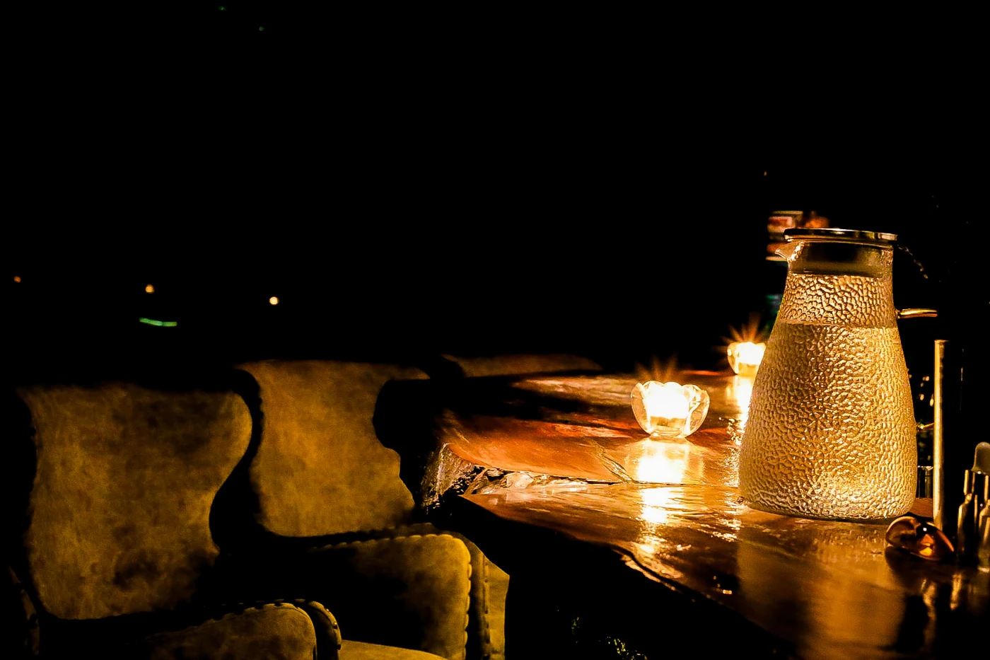 Candlelit wooden table with a textured water pitcher and upholstered seating.