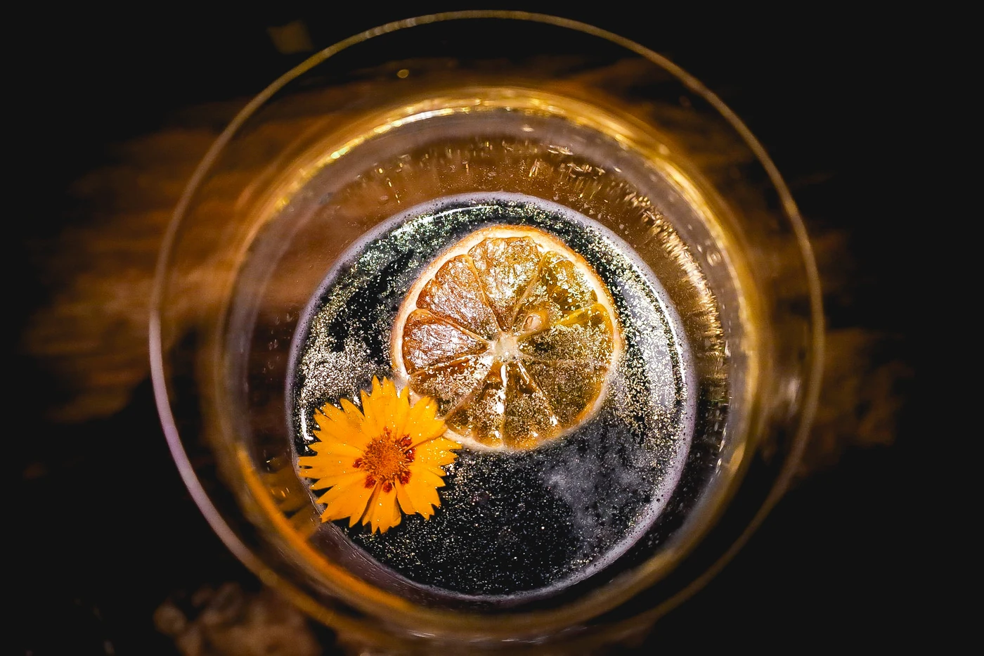 Cocktail viewed from above with a dried citrus wheel and a yellow flower.