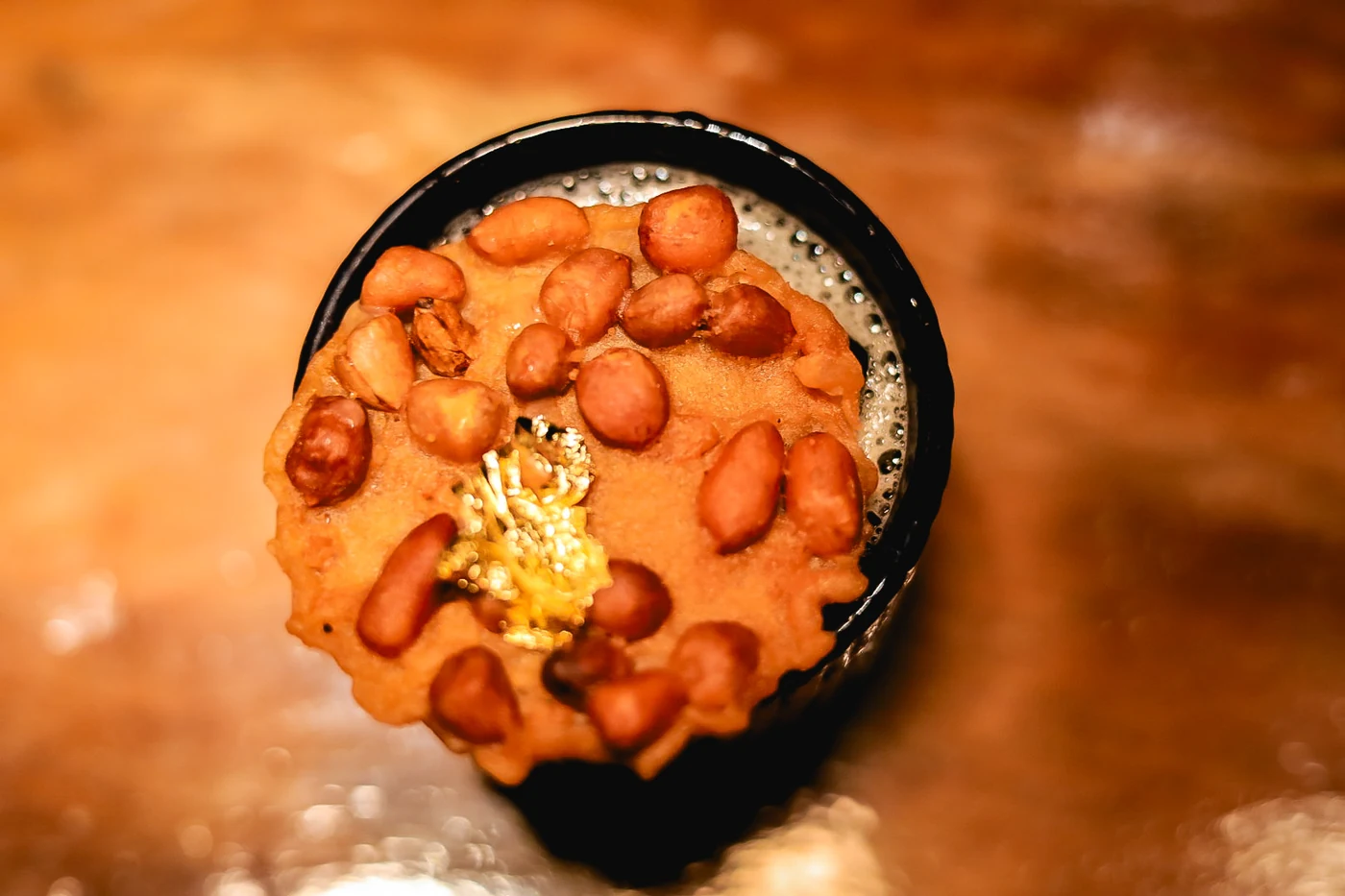 Cocktail viewed from above with a round nut-covered garnish on the warm wooden bar.